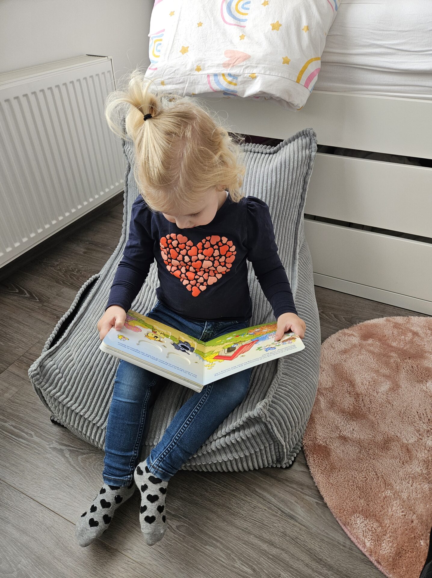 Klein meisje zit op een zacht stoelkussen en leest aandachtig in Woezel & Pip: Buitenspeeldag.