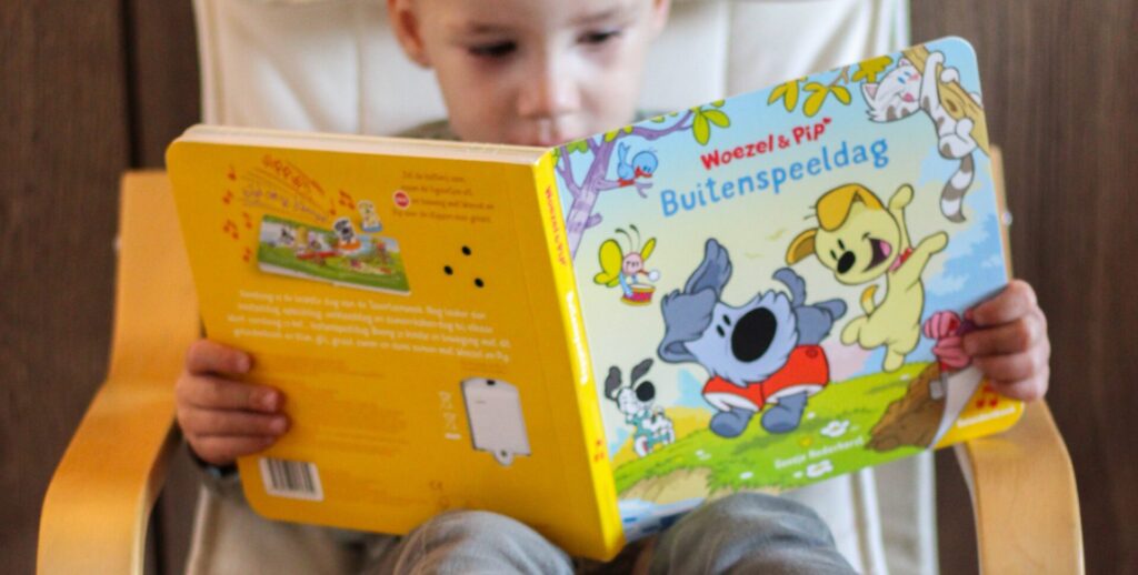 Jonge jongen zit geconcentreerd op een stoel en leest het boek Woezel & Pip: Buitenspeeldag als onderdeel van het Kinderboekjes.nl kinderpanel.