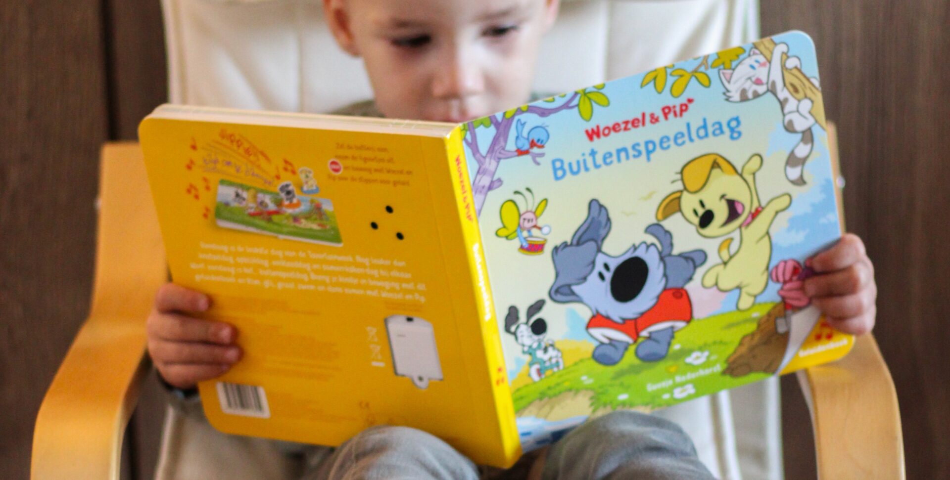 Jonge jongen zit geconcentreerd op een stoel en leest het boek Woezel & Pip: Buitenspeeldag als onderdeel van het Kinderboekjes.nl kinderpanel.