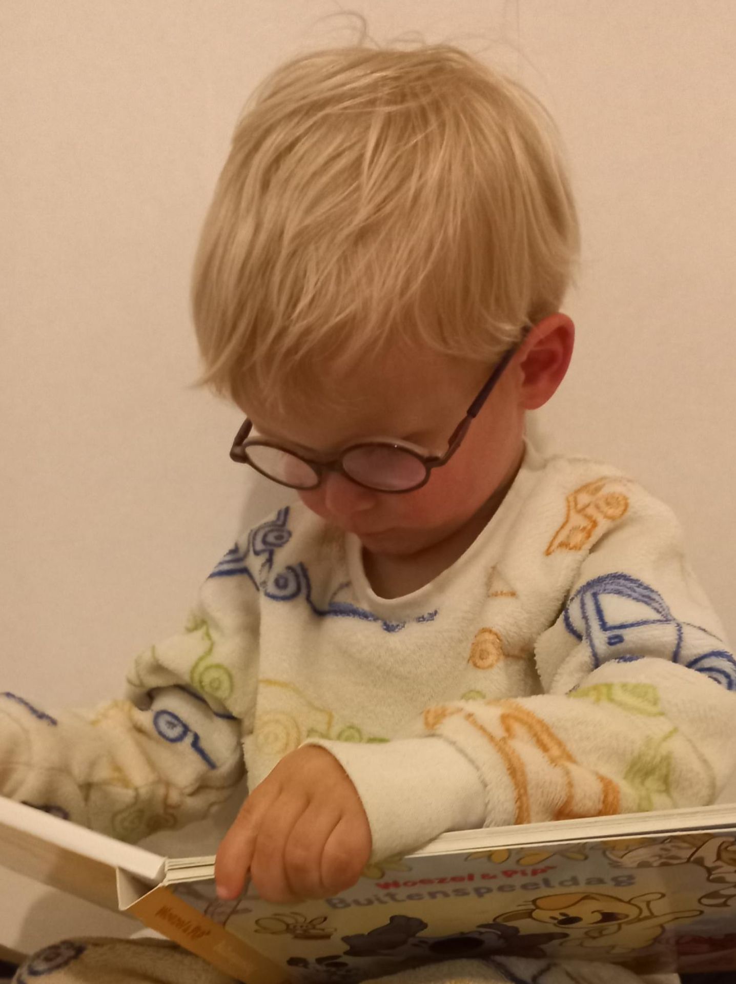 Peuter in pyjama met bril leest gefocust Woezel & Pip: Buitenspeeldag voor het slapengaan.