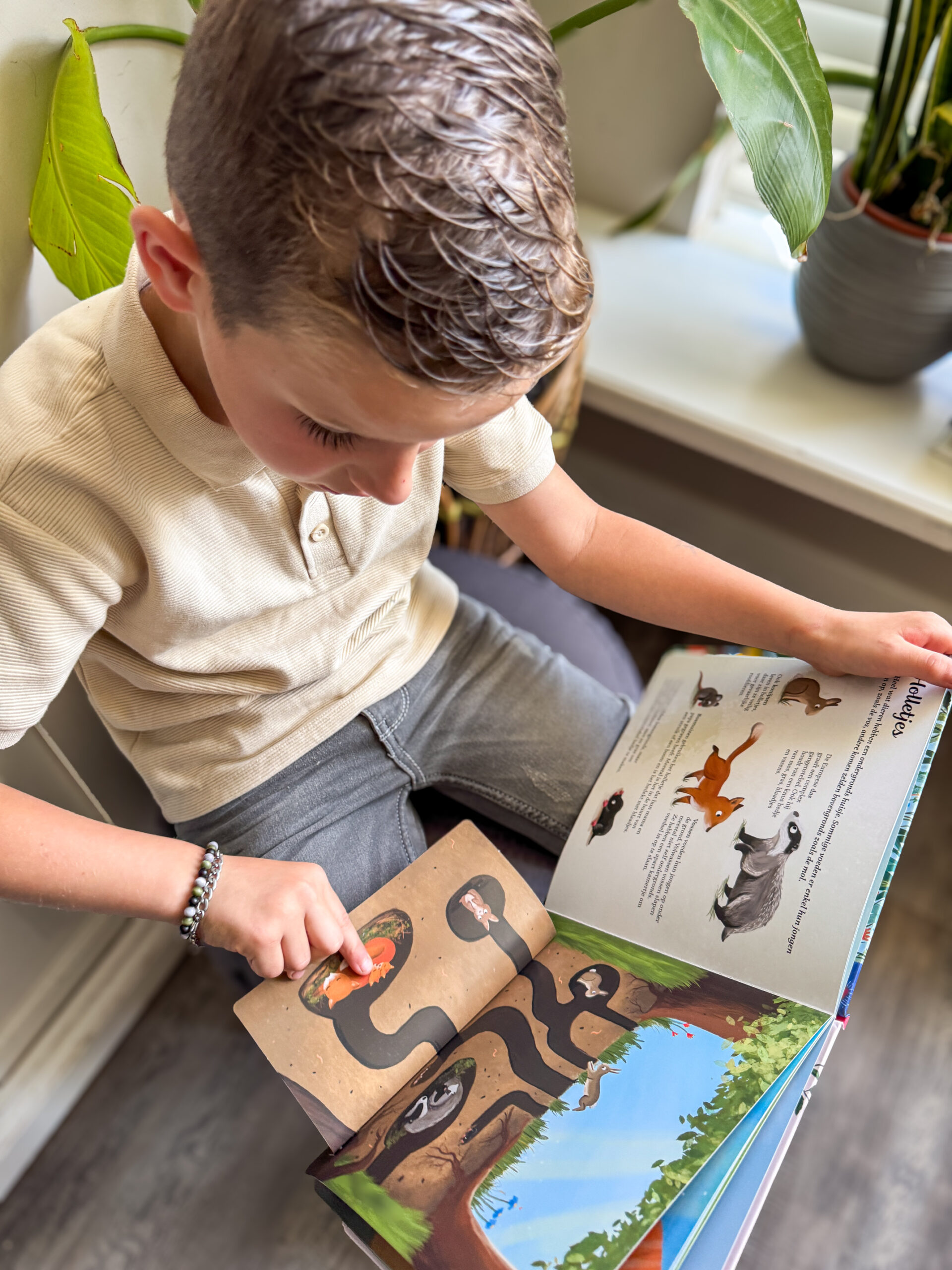 Jongen bladert geïnteresseerd in het boek “Ik ontdek de natuur” en tilt een flapje op bij een illustratie van ondergrondse dieren.