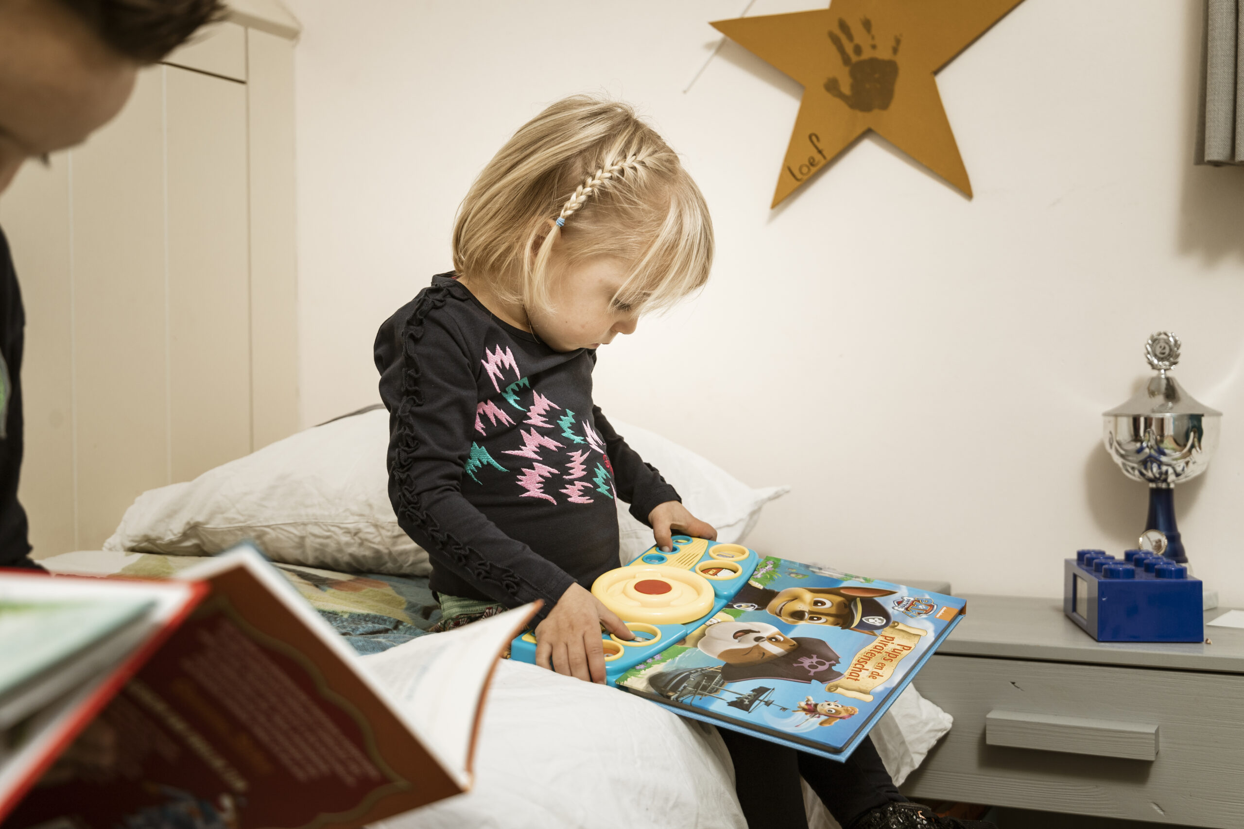 Kleuter zit op bed en leest geconcentreerd een Paw Patrol geluidenboek met kleurrijke knoppen en illustraties van de bekende pups.