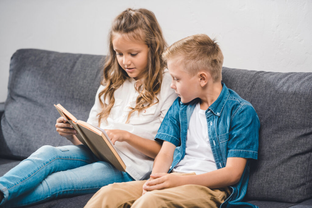 Twee kinderen lezen samen een kinderboekje op de bank als voorbereiding op de eerste schooldag.