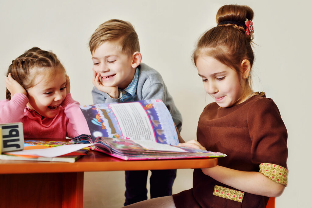 Drie kinderen lezen samen een kleurrijk boek over de wereld en lachen om de avonturen die ze onderweg tegenkomen.