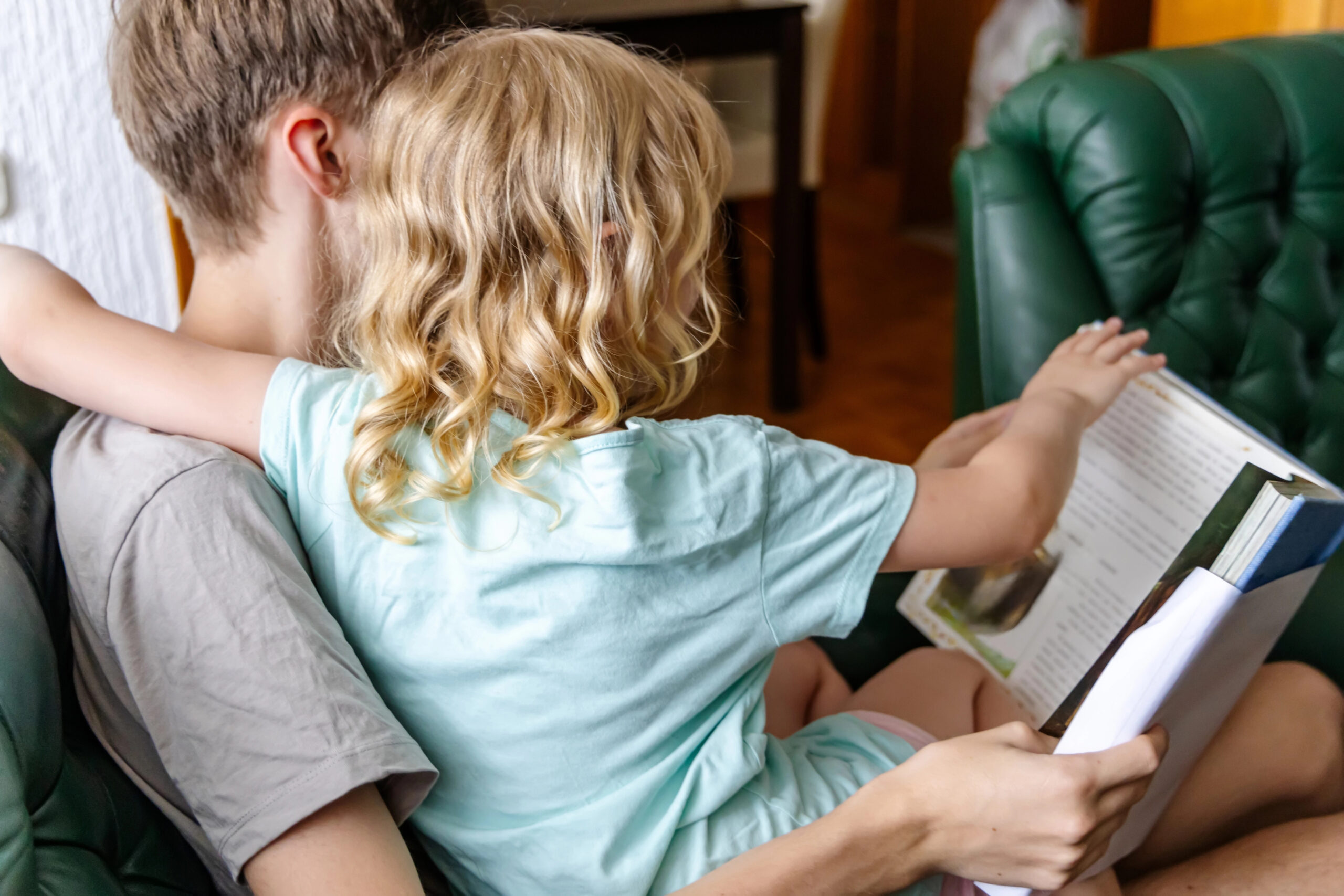 Peuter zit op schoot bij man op de bank en bladert nieuwsgierig mee in een groot kinderboek.